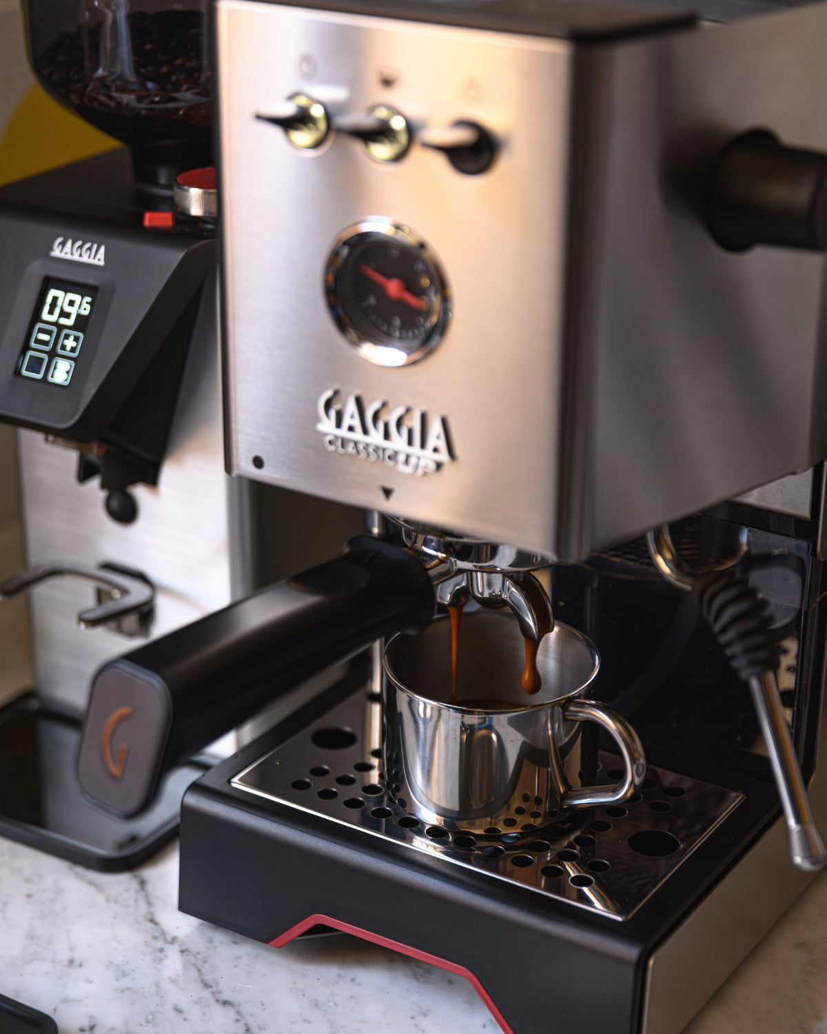 Gaggia Classic UP in Inox mit laufendem Espresso, daneben die Kaffeemühle MDF 55